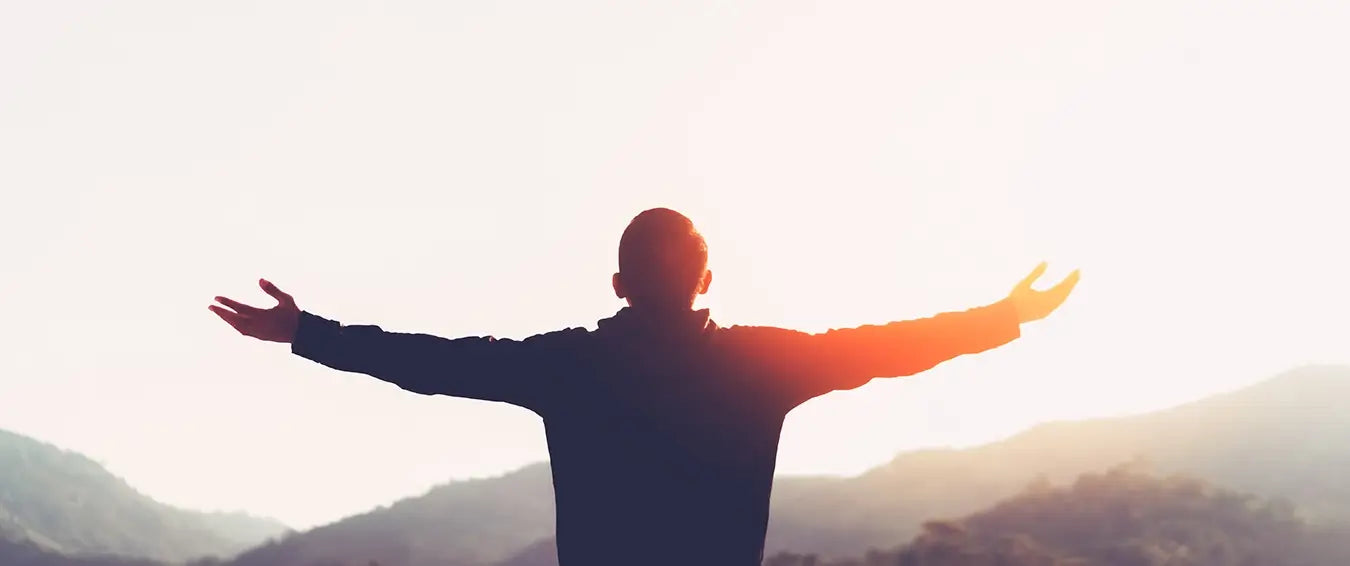 man with his arms open looking at the rising sun