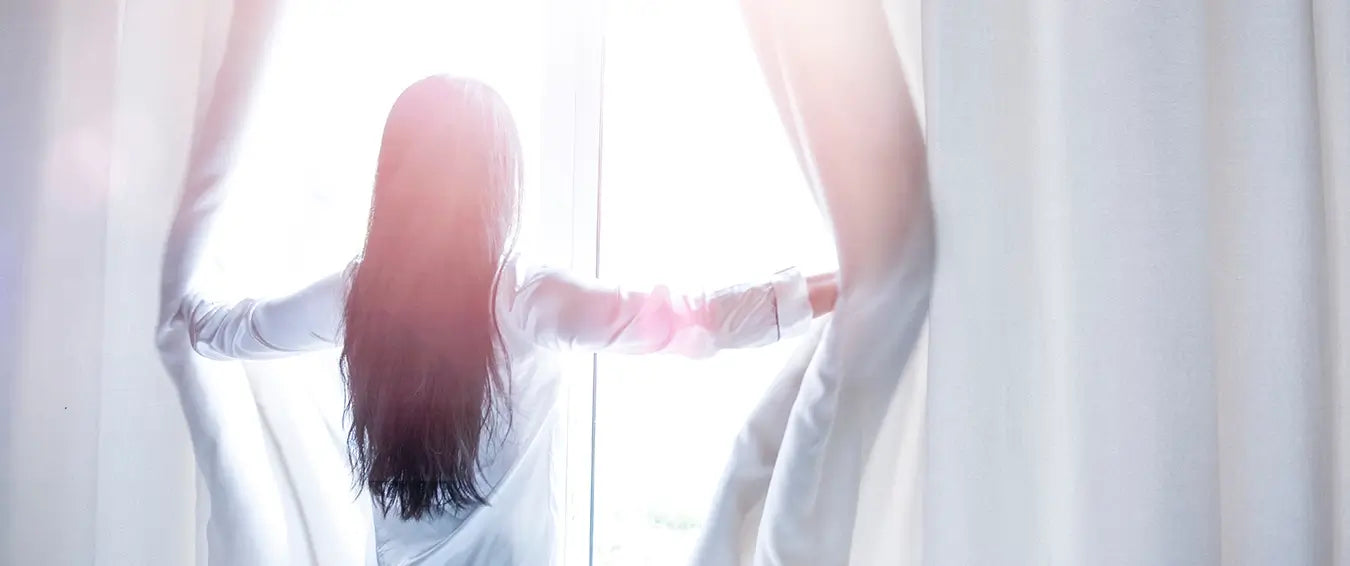 woman opening the curtains to let the sunshine in