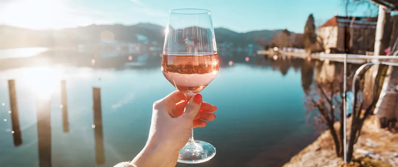 woman raising a glass of rosé by a lake