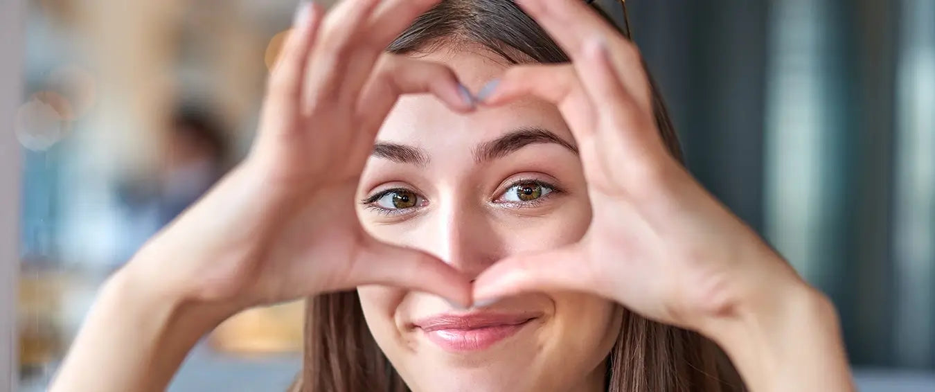 woman smiling at the camera throgh heart shape she makes with her hands