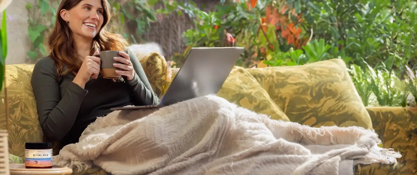 woman relaxing on the couch with a Live Conscious Beyond Brew beverage and her laptop