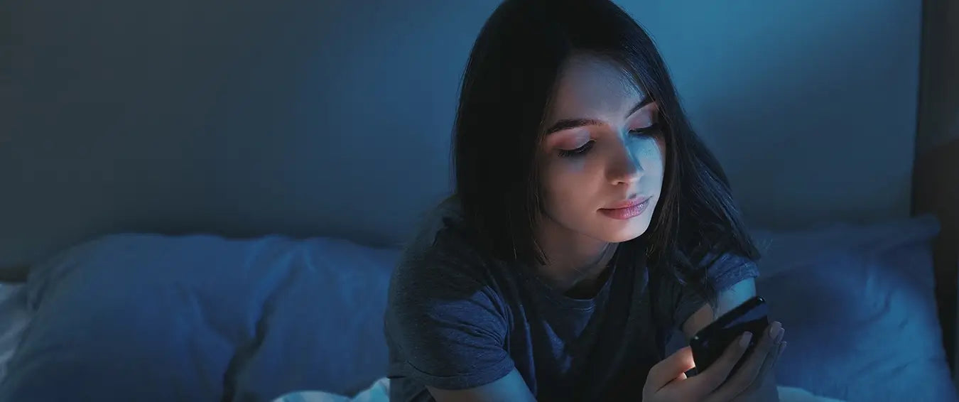 woman sitting on bed looking at her phone