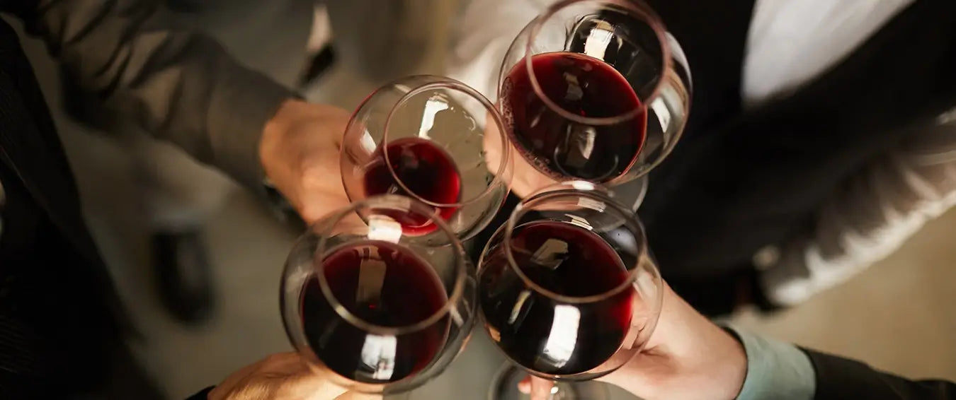 four individuals cheering with glasses of red wine