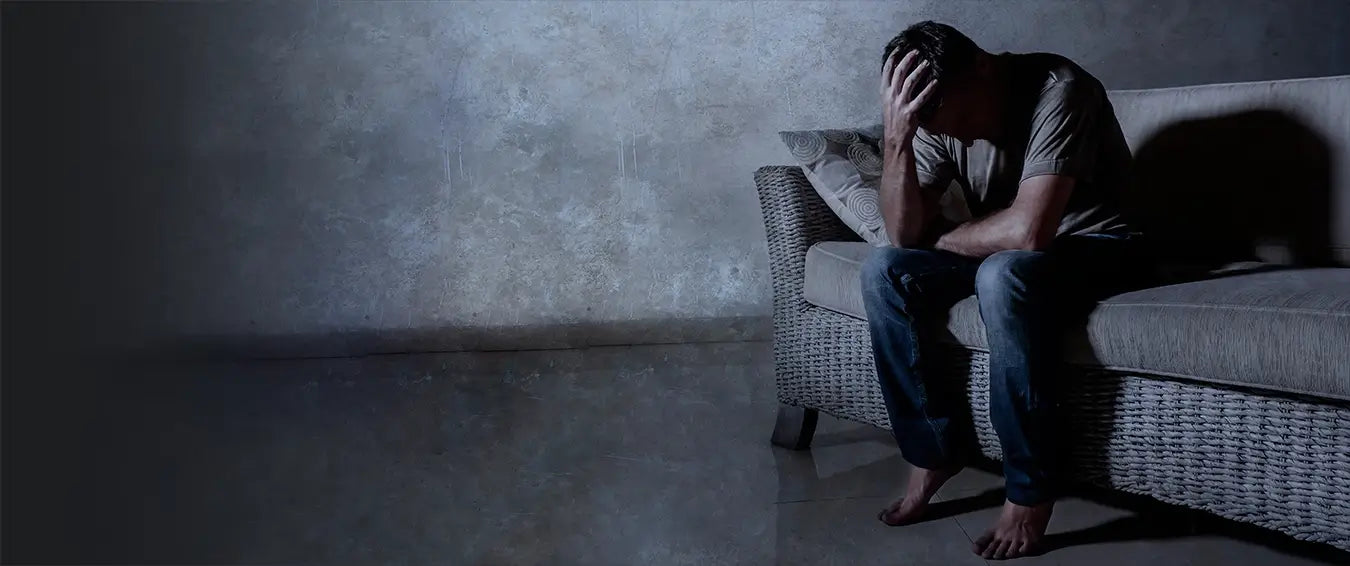 man holding his head on a couch in a dark room