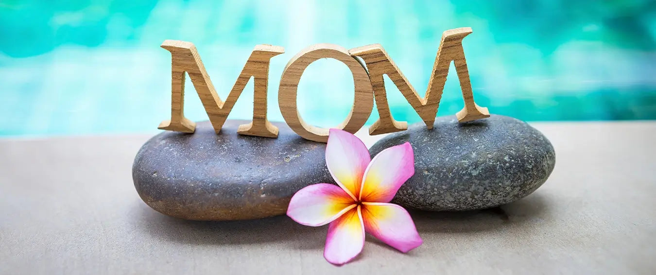 a flower in front of two large pebbles carrying wooden letter spelling mom by the pool