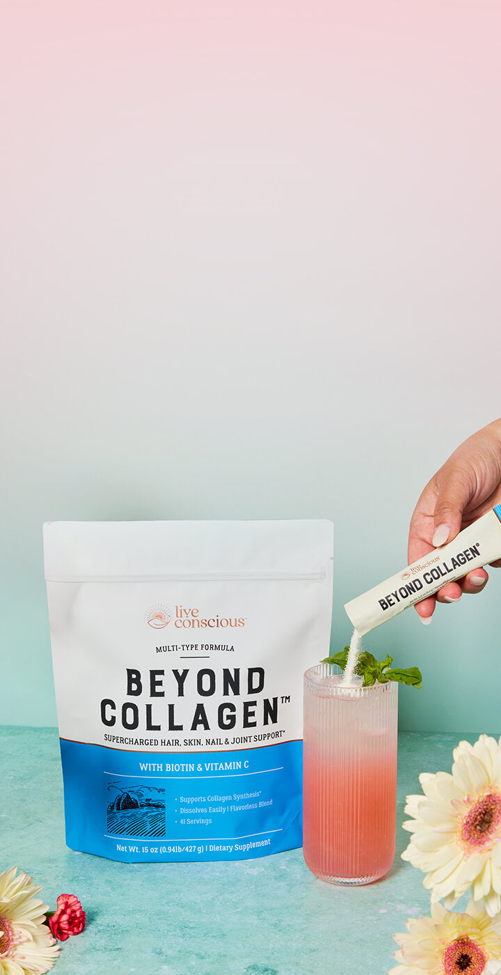 A hand pours a white powder stick from a Beyond Collagen tube into a pink drink with mint, next to a large bag of Beyond Collagen on a pastel blue and pink background with decorative flowers.